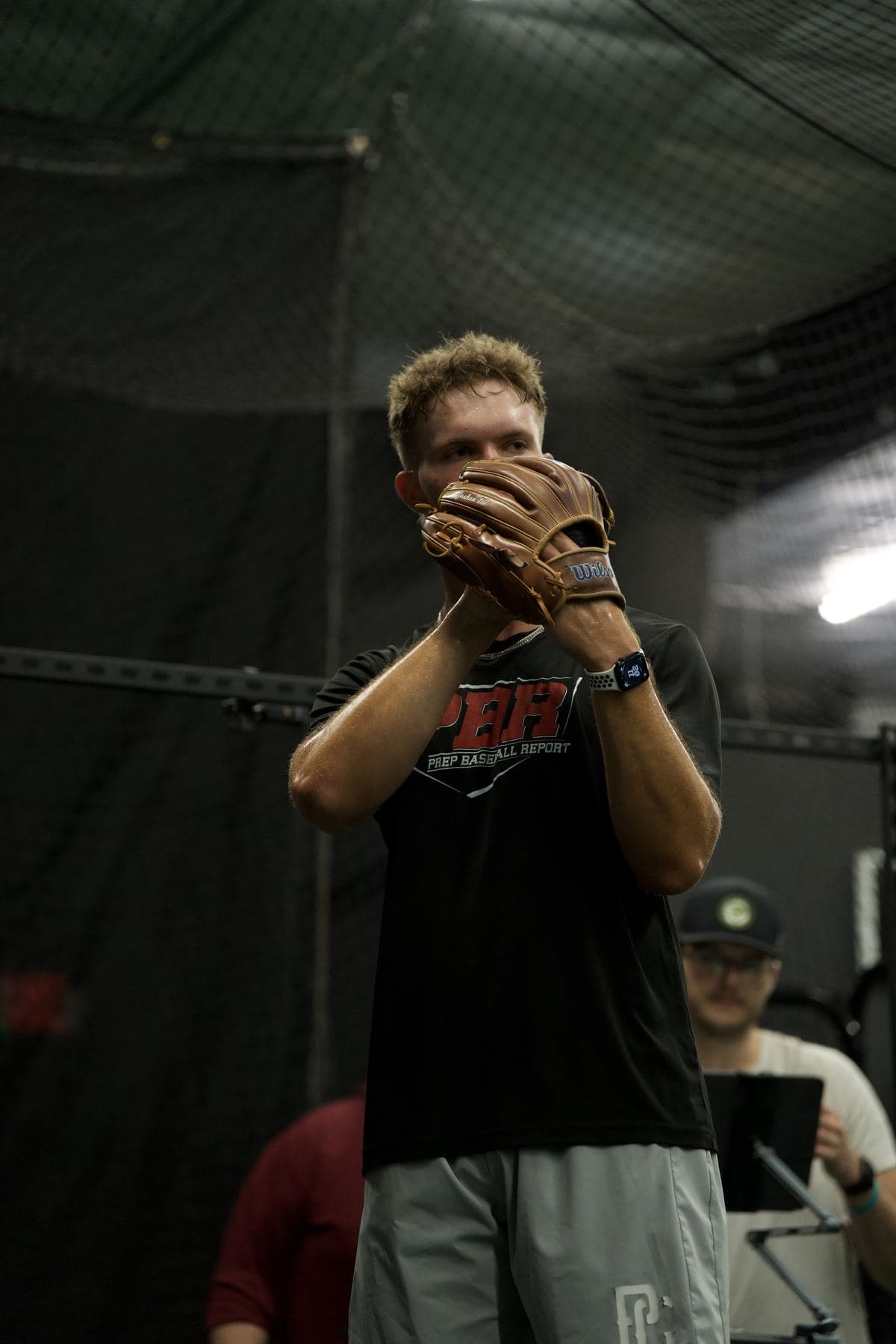 A pitcher set at the top of his delivery while a PPL coach watches from behind